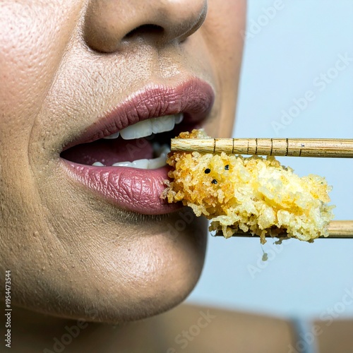 A detailed close-up shot of a woman with pinkish lips about to take a bite of a golden, crispy, deep-fried breaded snack held by wooden chopsticks