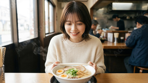 Smiling young Japanese woman looking at a hot bowl of ramen with steam and toppings