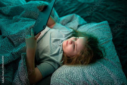 Фотография Teenager distracted by tablet screen in bed at night