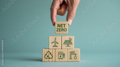 Hand Placing NET ZERO Block On Stacked Wooden Blocks With Eco-Friendly Symbols For Sustainable Energy And Climate Change Concepts