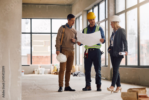 Building site foreman analyzing blueprints with project managers at construction site.