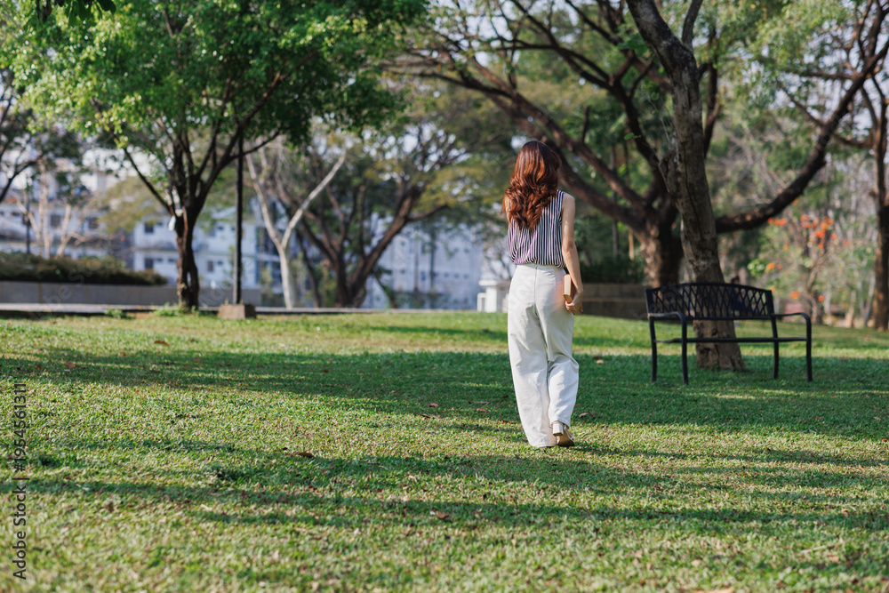 Fototapeta premium Young woman walking away in green park exploring nature
