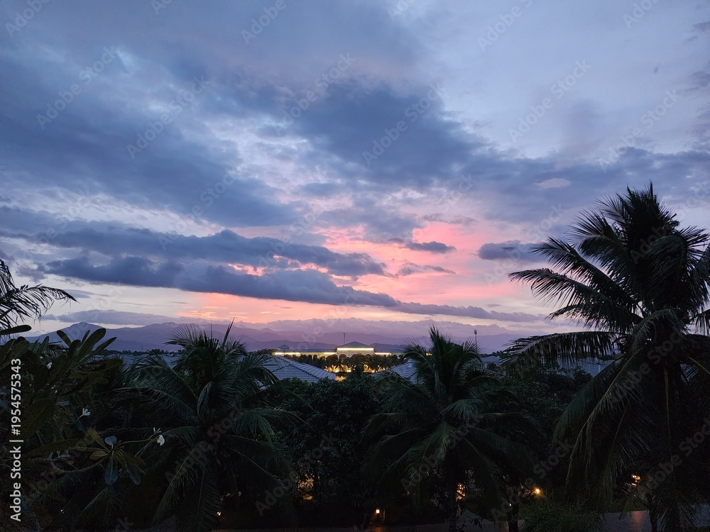 Obraz premium Tropical Sunset with Pink Clouds and Palm Tree Silhouettes over Mountain Range 산맥 위로 펼쳐진 분홍빛 노을 구름과 야자수 실루엣의 열대 풍경