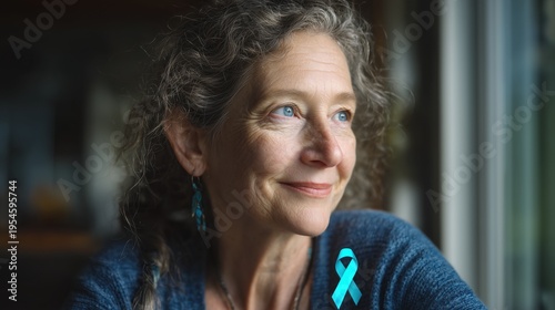Oral, Head and Neck Cancer Awareness Week:a middle-aged woman survivor smiling with quiet strength, sitting near a bright window with natural light, wearing a teal awareness ribbon pin on her shirt