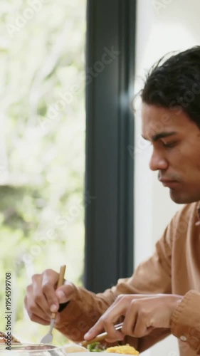 Vertical video: Cutting brown shirt man starting meal, eating with fork, knife at home, copy space