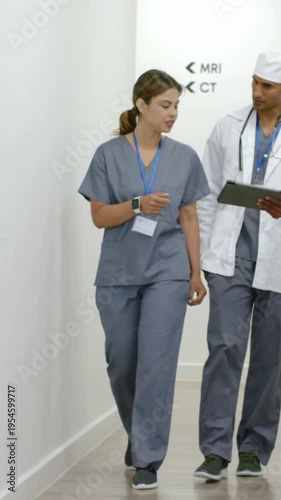 Vertical video: Walking scrub nurse and MD in coat holding tablet checking scan data by MRI CT sign