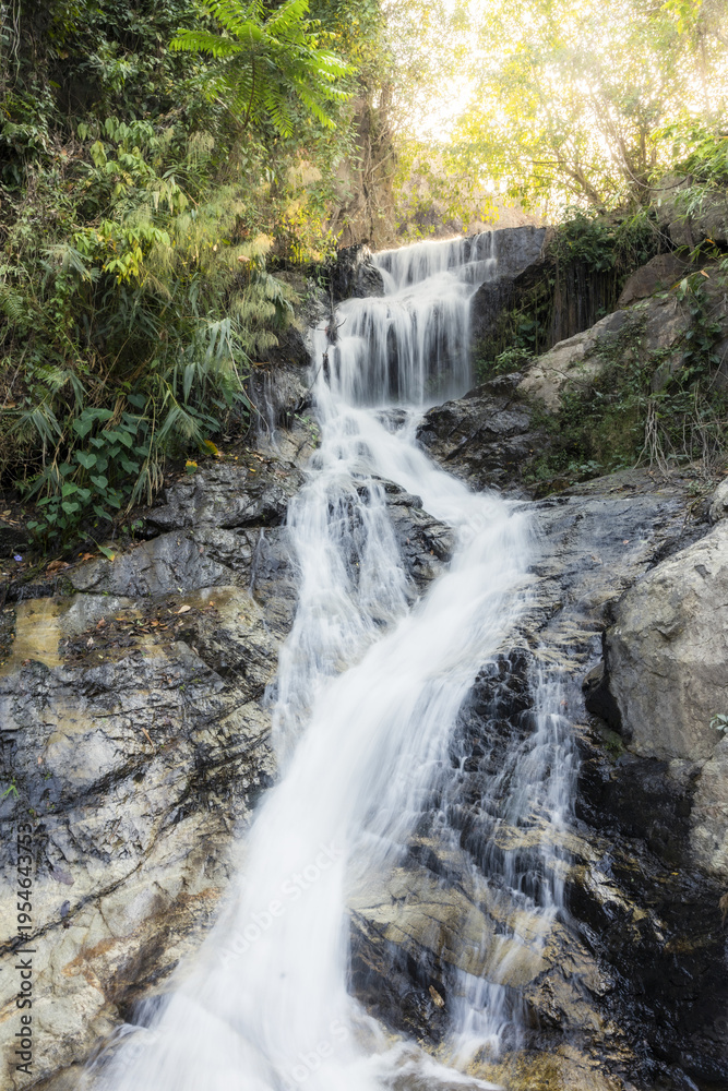 Fototapeta premium Beautiful natural waterfall cascading down rocky cliff in lush green forest creating serene peaceful and calming atmosphere perfect for relaxation