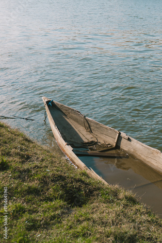 Old wooden dugout canoe partially submerged at the grassy riverbank on a sunny day