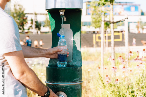 Картината върху платно Man refilling plastic water bottle at public drinking fountain in city park