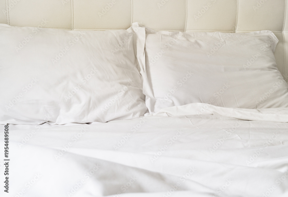 Obraz premium White bed with pillows and clean sheets on a simple headboard in a bright room