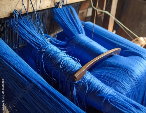 Close-up of a wooden loom, featuring vibrant blue threads, partially in focus. The tool rests amid the dense textile work