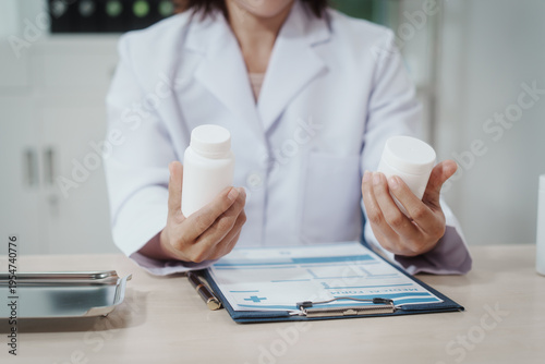 Doctor in white coat holding two medicine bottles over clipboard on desk in clinic, comparing prescription options, healthcare consultation concept.