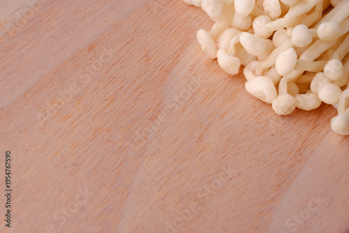 Fresh enoki mushroom on wooden cutting board. Raw food ingredient with copy space on rustic wooden background.