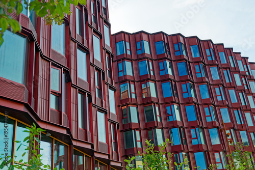 Foto Modern red building facade with large blue reflective windows and green foliage