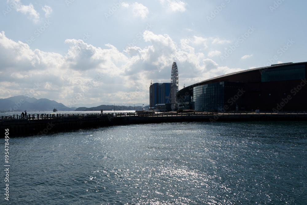Fototapeta premium Panoramic coastal view of Shimonoseki Kaikyokan Aquarium and Ferris wheel with bright sun reflecting on the sea waves.