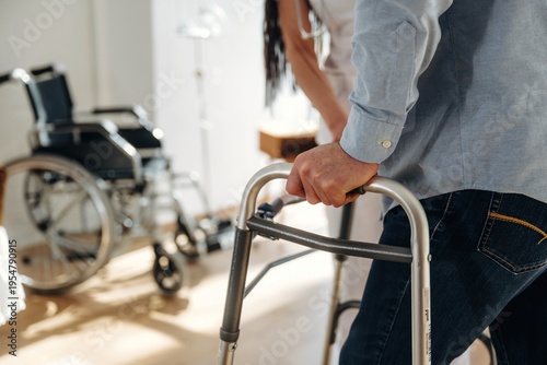 Wallpaper Mural Individual using a walker for support while standing in a bright room with a wheelchair and medical equipment visible in the background Torontodigital.ca