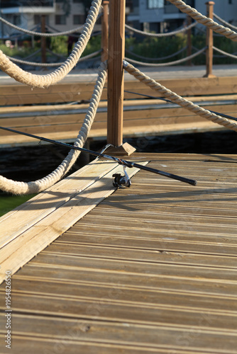 A fishing rod on a wooden pier with a rope railing. Relaxation concept. Selective focus.