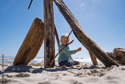 Little 4 year old girl playing with wooden sticks on a sandy beach