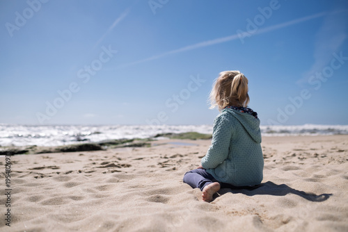 Little 4-year-old girl relaxing on a quiet beach during springtime