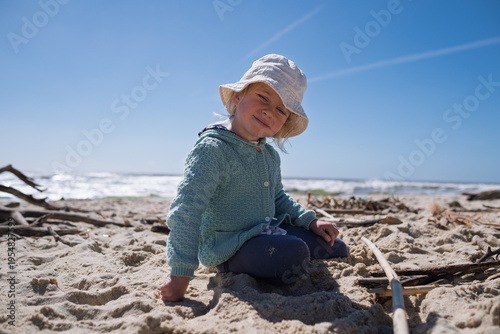 Little 4 year old girl playing with wooden sticks on a sandy beach