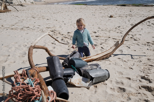 Little 4 year old girl playing with wooden sticks on a sandy beach