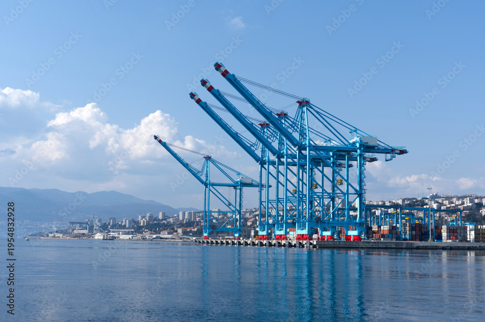 Obraz premium Large commercial port with blue container cranes on waterfront — global shipping logistics, maritime infrastructure, cargo terminal aerial view