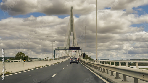 Dramatic perspective of the tall white bridge pylon and cables rising above the motorway over the Guadiana River.