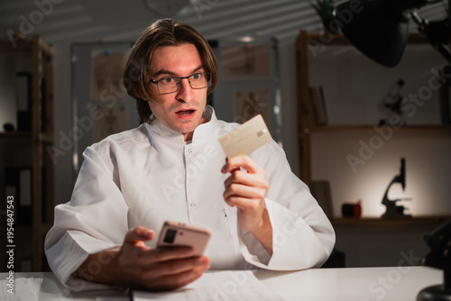 Shocked doctor with credit card payment from his mobile Phone using banking app during night shift at hospital. healthcare, online shopping and e-commerce