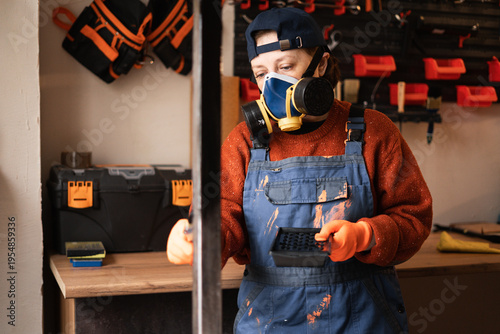 Konstfotografi Female Worker in overalls and mask respirator painting metal construction in industrial workshop