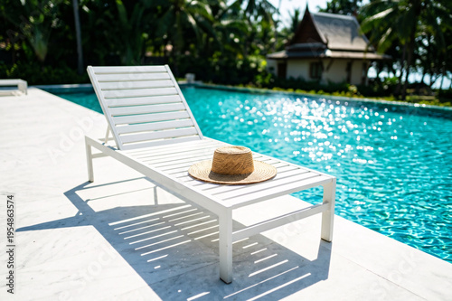 Straw Hat on White Lounger by Luxury Swimming Pool at Tropical Resort