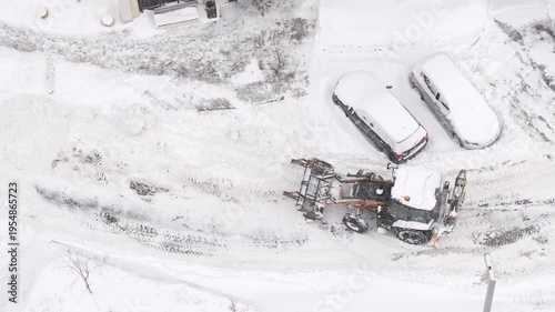 Aerial drone view of snow removal machinery clearing road in winter industrial area, heavy equipment working in harsh weather conditions