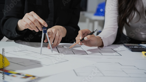 Two architects drafting building floor plans on a table using compass and pencil, close-up of hands and architectural drawings