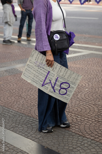 Mujer en la marcha de la mujer sosteniendo un cartel con partituras musicales y el 8m escrito en el. Mujer vestida de violeta en la marcha por los derechos de las mujeres. 