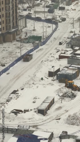 Snow-covered construction site with machinery and materials, winter urban scene, industrial city landscape, construction activity, cold winter atmosphere