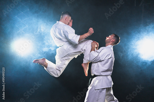 Martial arts masters on dark background. Strong man fighters in white kimono for karate martial arts fighting training in black gym. Karate fighters training punches kicks practicing fight sparring