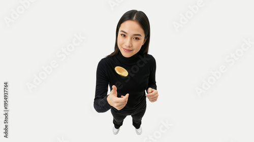 High angle view of a smiling young Asian woman tossing a gold coin. Female investor flipping a coin on a white background. Cryptocurrency and finance concept