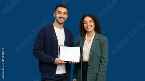 Smiling diverse couple holding a blank tablet screen. Man and woman presenting digital pad mockup on blue background. Copy space for text