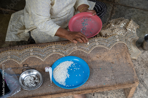 Indian woman making traditional beadwork jewelry, close-up of hands with colorful beads and handcrafted textile