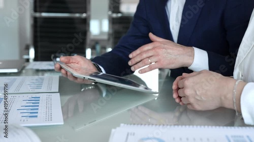 Business partners collaborating on a digital tablet, analyzing financial data and reports during a corporate meeting in a modern office, planning strategies for growth