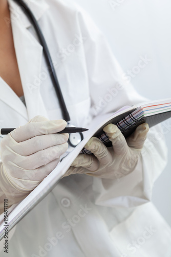 Female medical worker writing notes, wearing gloves and a stethoscope