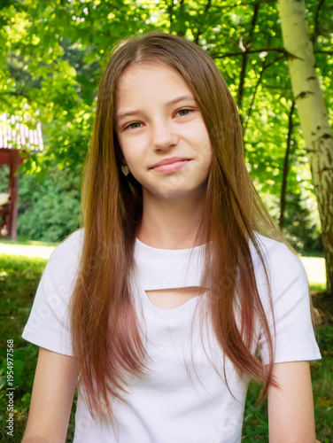 Young girl with long hair looking at camera in park. Portrait of beautiful child outdoors. Summer lifestyle, natural beauty and happiness in nature. Casual clothing, sunny day concept.