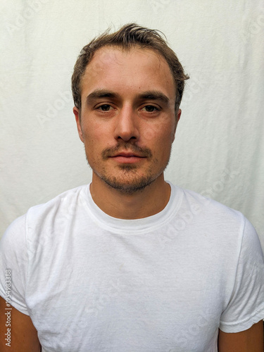 A portrait of a tanned young man wearing a white shirt with a white background and looking at the camera.