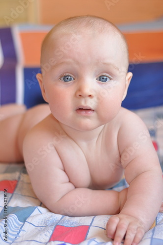 Fotografie Baby with inquisitive expression lying on a bright patterned bedspread