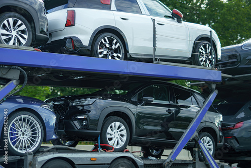 During the daytime, a truck is actively engaged in loading and transporting cars at a bustling transport operations area