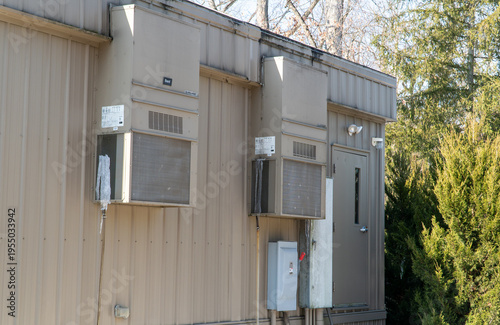 Fotografie Exterior view of a modular office building with beige corrugated metal siding, featuring two Bard WALL-MOUNT HVAC units, one with icicles, an electrical disconnect, and a utility door