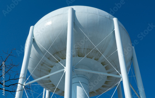 Iconic white elevated water tower against a brilliant clear blue sky, viewed from below, showcasing vital utility infrastructure and a symbol of municipal water supply in a town.