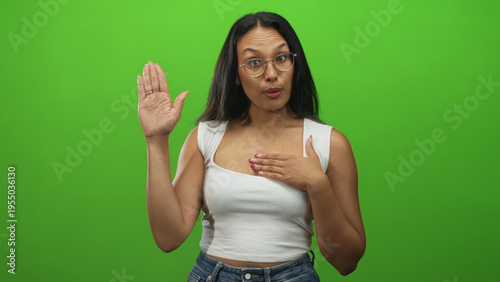 Fotografía Woman with glasses in white tanktop raising right hand and placing left hand over chest in studio greenscreen, speaking as if taking an oath; commitment solemn