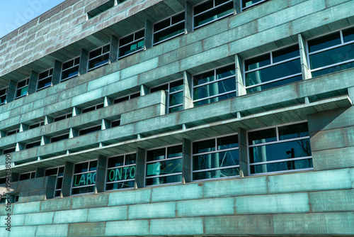 Vászonkép Modern building facade with weathered verdigris copper cladding and geometric window patterns under a clear blue sky, showcasing unique patina texture and contemporary architectural design