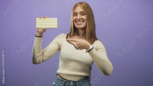 Young woman holding white chocolate bar points finger toward camera in studio; playful product promotion campaign.
