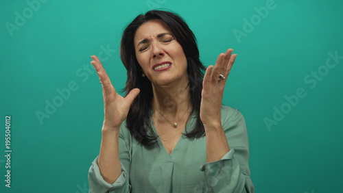 Bild auf Leinwand Middle aged woman raises hands to face in teal studio setting with expressive gesture and closed eyes showing despair; frustration